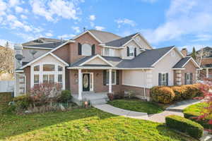 Traditional home featuring a front yard, brick siding, stucco siding, covered porch, and roof with shingles