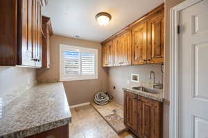 Laundry area featuring hookup for an electric dryer, stone tile floors, hookup for a washing machine, and cabinet space