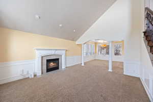 Unfurnished living room with arched walkways, wainscoting, a decorative wall, carpet floors, and decorative columns