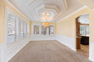 Unfurnished dining area featuring crown molding, a decorative wall, plenty of natural light, arched walkways, and light colored carpet