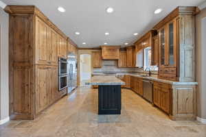 Kitchen featuring brown cabinets, a center island, glass insert cabinets, light stone countertops, and recessed lighting