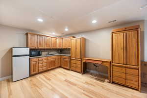 Kitchen with freestanding refrigerator, black microwave, recessed lighting, decorative backsplash, and light wood finished floors
