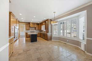 Kitchen with a kitchen island, stone tile floors, pendant lighting, brown cabinetry, and crown molding