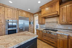 Kitchen featuring built in appliances, brown cabinets, arched walkways, and recessed lighting