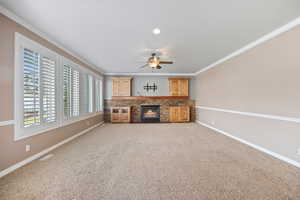 Unfurnished living room with crown molding, light colored carpet, a fireplace, and ceiling fan