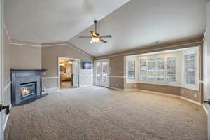 Unfurnished living room with a tiled fireplace, lofted ceiling, a ceiling fan, and carpet