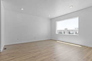Spare room featuring light wood-type flooring, a textured ceiling, and recessed lighting