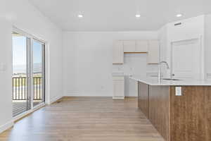 Kitchen with light wood-type flooring, recessed lighting, light stone countertops, brown cabinetry, and white cabinetry
