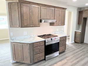 Kitchen with gas range, light countertops, under cabinet range hood, and light wood-style flooring
