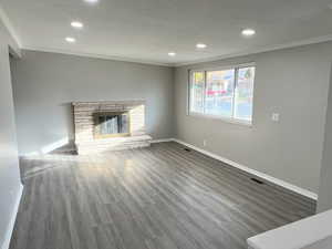 Unfurnished living room with recessed lighting, wood finished floors, crown molding, and a glass covered fireplace