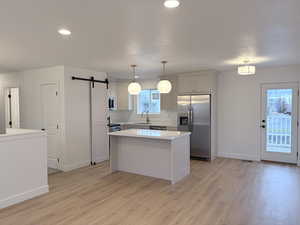 Kitchen with a barn door, appliances with stainless steel finishes, a center island, hanging light fixtures, and white cabinets