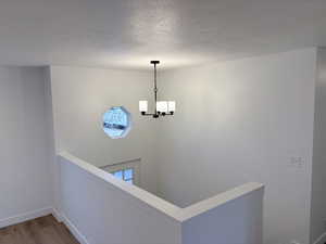 Hallway featuring a textured ceiling, wood finished floors, a chandelier, and an upstairs landing