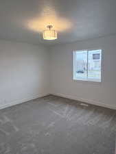 Empty room featuring a textured ceiling and dark colored carpet