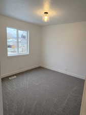 Empty room featuring a textured ceiling and dark colored carpet