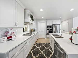 Kitchen featuring appliances with stainless steel finishes, white cabinetry, custom exhaust hood, light stone countertops, and light wood-style flooring