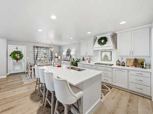 Kitchen featuring white cabinets, light wood-style floors, a breakfast bar, decorative backsplash, and a center island with sink