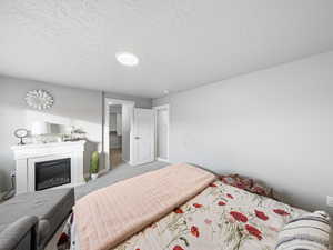Carpeted bedroom featuring a textured ceiling and a glass covered fireplace