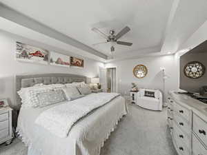 Master Bedroom with a raised ceiling, light colored carpet, ceiling fan, and a textured ceiling