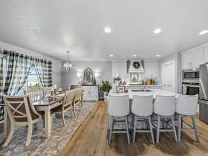 Kitchen featuring a textured ceiling, stainless steel appliances, a center island with sink, white cabinets, and light stone countertops
