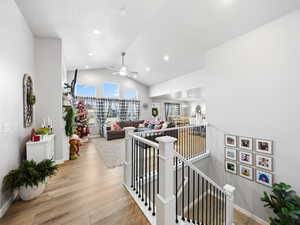 Hallway with an upstairs landing, lofted ceiling, light wood-style flooring, and recessed lighting