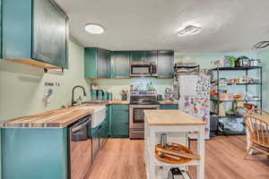 Kitchen with wooden counters, stainless steel appliances, light wood-style flooring, and green cabinets