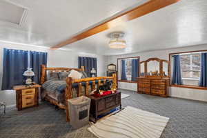Bedroom featuring a textured ceiling, dark carpet, and attic access