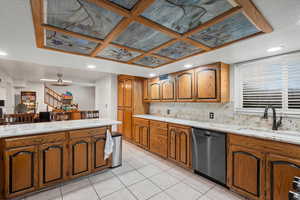 Kitchen with brown cabinetry, light stone countertops, dishwasher, light tile patterned floors, and recessed lighting