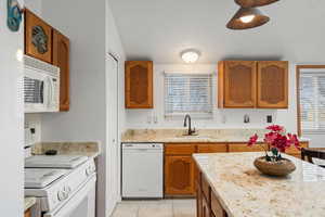 Kitchen with brown cabinets, white appliances, light stone countertops, and light tile patterned flooring