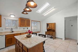 Kitchen featuring a skylight, lofted ceiling, brown cabinets, light tile patterned floors, and a kitchen bar