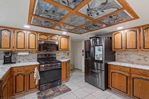 Kitchen with stainless steel appliances, light stone counters, brown cabinetry, light tile patterned flooring, and decorative backsplash
