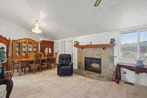 Living room with a stone fireplace, tile patterned floors, lofted ceiling, a ceiling fan, and a textured ceiling