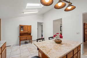 Kitchen featuring brown cabinetry, a kitchen bar, lofted ceiling, light tile patterned floors, and a skylight