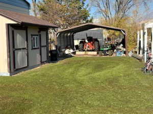 View of grassy yard featuring a detached carport and an outbuilding