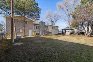 Rear view of house featuring a gazebo, brick siding, a chimney, and a yard