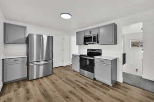 Kitchen with gray cabinetry, stainless steel appliances, light countertops, and light wood-style floors