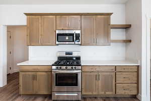 Photo of home built in past by OLO. Kitchen featuring appliances with stainless steel finishes, open shelves, light countertops, and dark wood-style flooring