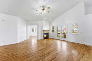 Unfurnished living room featuring high vaulted ceiling, light wood finished floors, a ceiling fan, and a glass covered fireplace