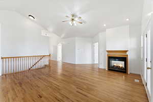 Unfurnished living room with light wood-style floors, a glass covered fireplace, arched walkways, a ceiling fan, and vaulted ceiling