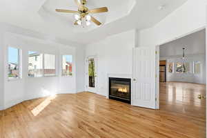 Unfurnished living room with ceiling fan, a glass covered fireplace, light wood-style floors, and a raised ceiling