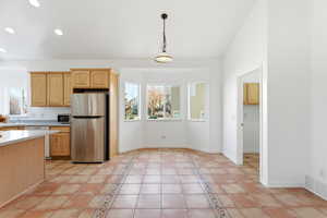 Kitchen featuring light countertops, light brown cabinetry, freestanding refrigerator, light tile patterned floors, and hanging light fixtures