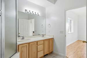 Primary Bathroom with double vanity, light tile patterned floors, and an enclosed shower and tub combo.