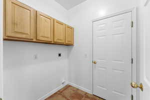 Laundry area with cabinet space, hookup for an electric dryer, and light tile patterned floors