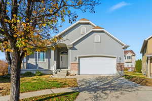 View of front of home with stucco siding, driveway, brick siding, a front lawn, and a garage