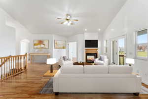 Virtually staged great room, featuring healthy amount of natural light, a glass covered fireplace, arched walkways, high vaulted ceiling, and light wood finished floors