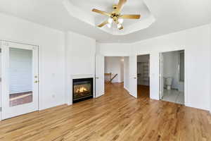 Unfurnished living room with a raised ceiling, light wood-style flooring, a glass covered fireplace, and ceiling fan. door to back deck.