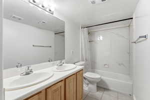 Full bath featuring double vanity, shower / tub combo, a textured ceiling, and light tile patterned flooring