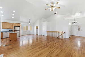 Unfurnished great room with light wood-type flooring, high vaulted ceiling, a chandelier, and ceiling fan