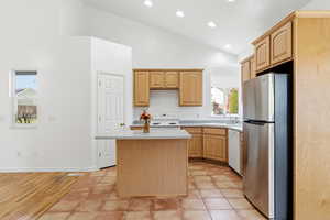 Kitchen with light brown cabinets, white appliances, a center island, light tile patterned floors, and high vaulted ceiling