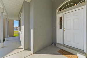 Covered front porch, wrap around, Doorway to property with stucco siding and a porch