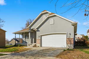 View of front of house with driveway, brick siding, stucco siding, and covered porch